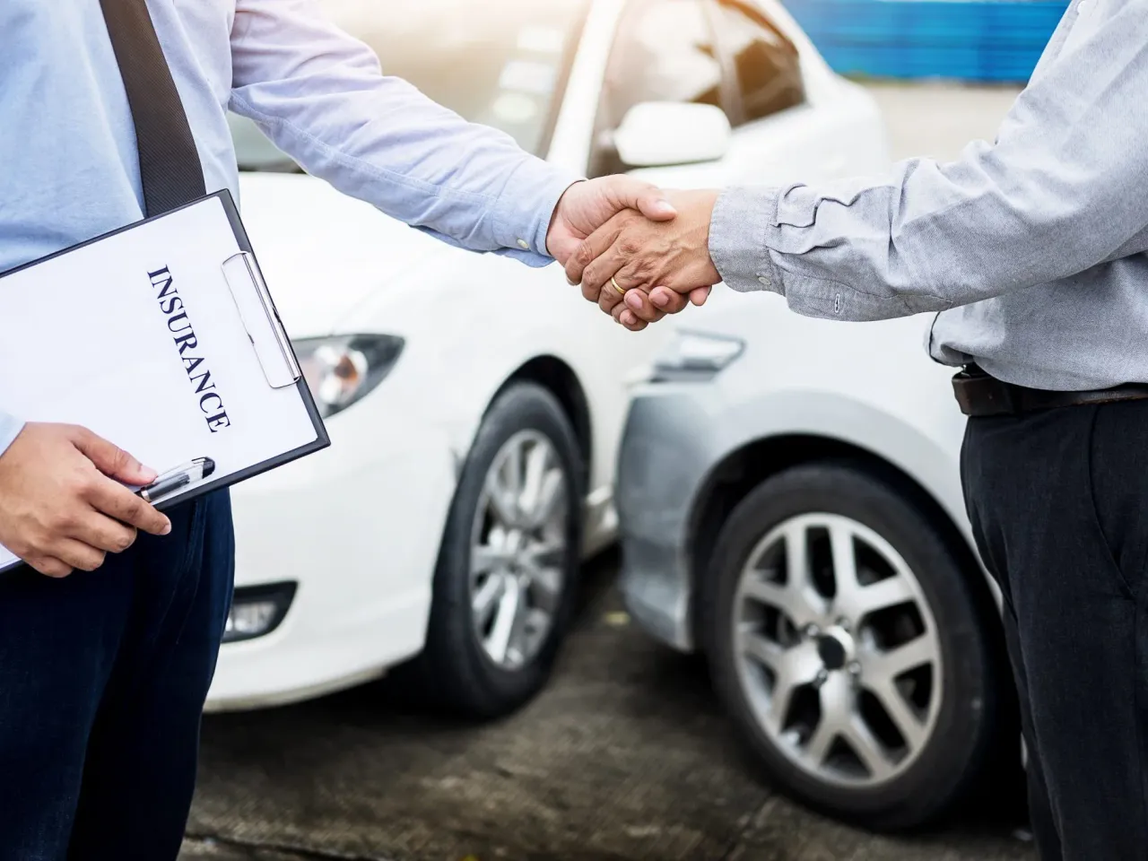 Agente de seguros estrechando la mano de un cliente junto a un auto